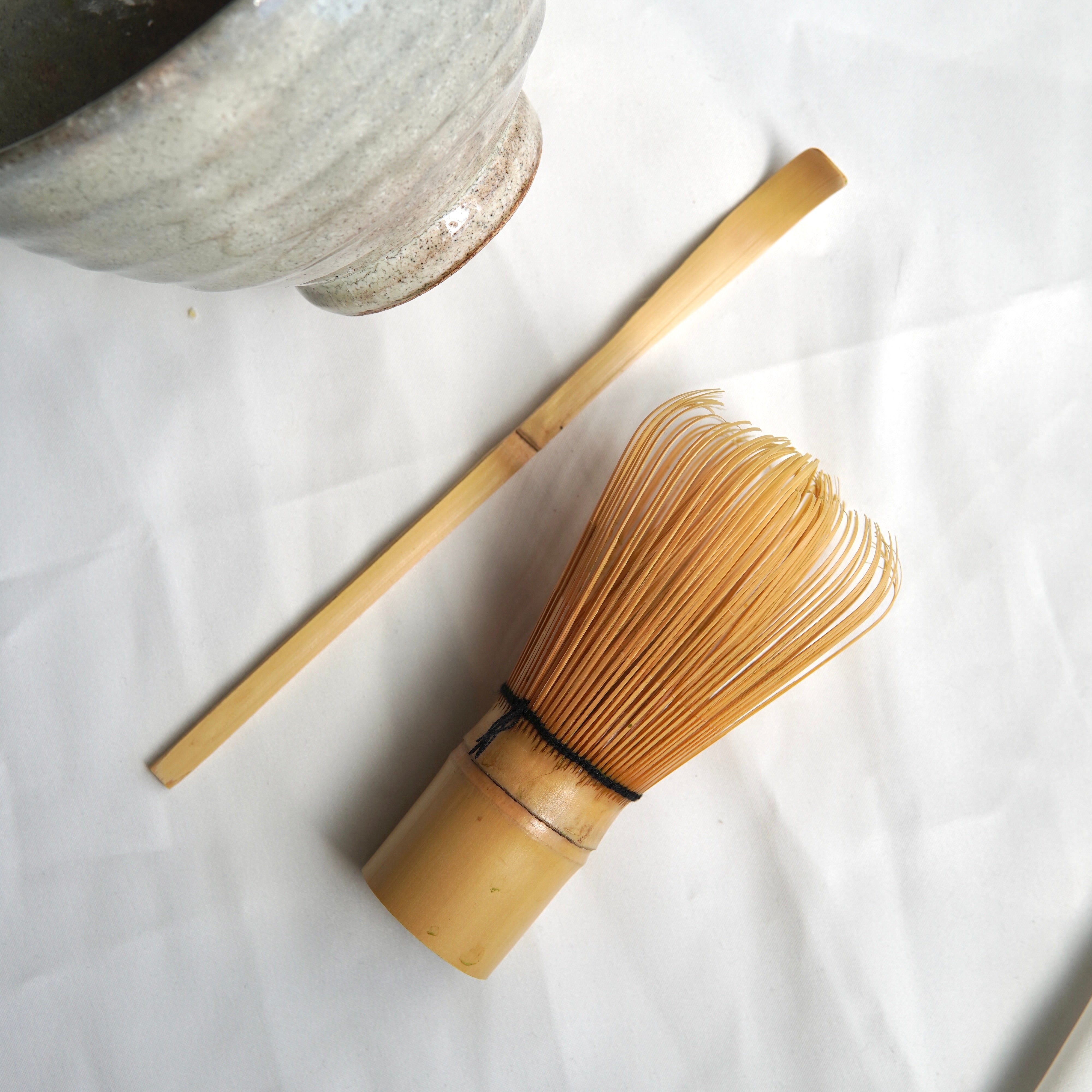Ein handgefertigtes Matcha-Set von Luke Jaque Rodney Store mit Bambuslöffel, Matchabesen und Matcha-Schale liegt auf weißem Tuch - essentielle Utensilien für die japanische Teezeremonie.