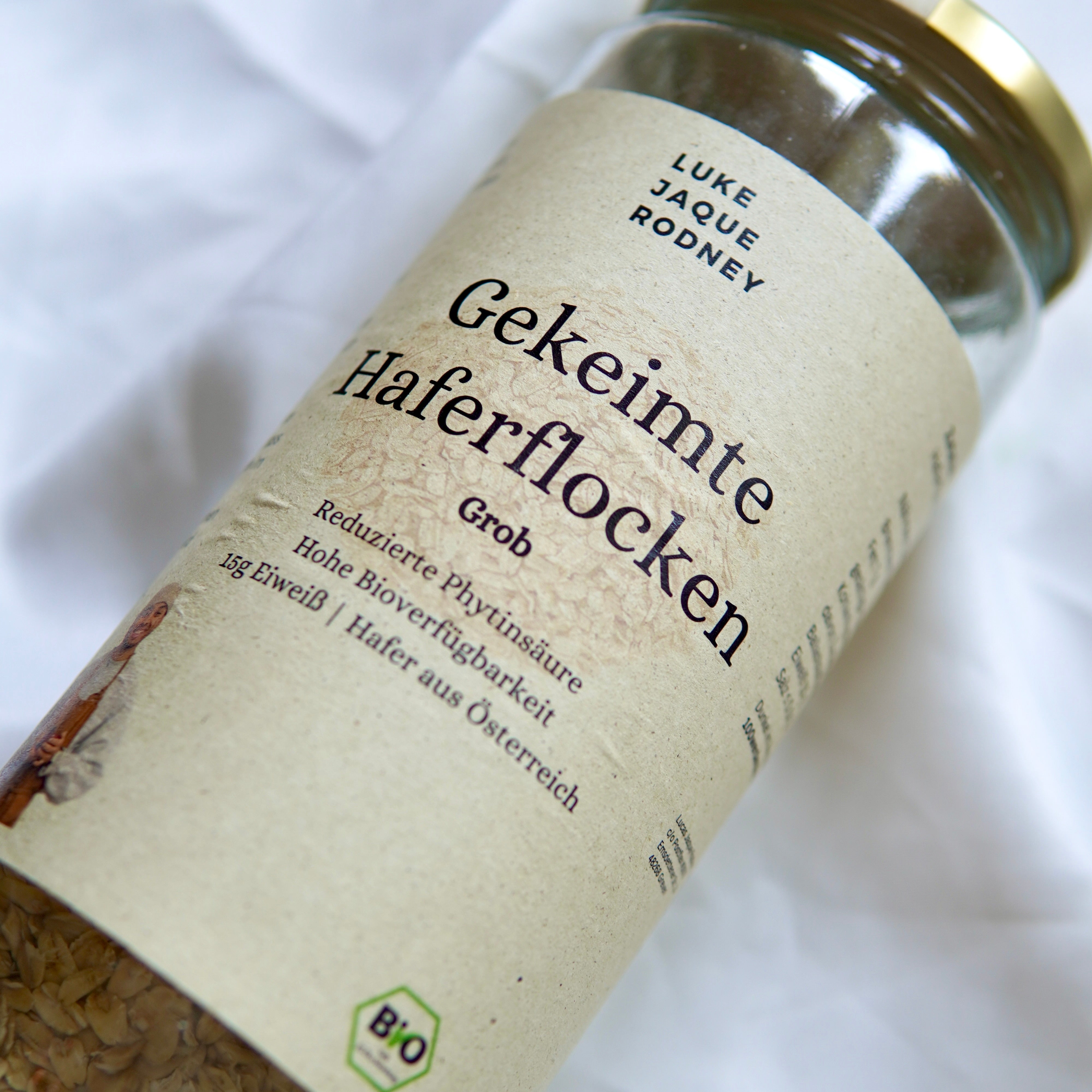 Eine Nahaufnahme einer Dose Gekeimte Haferflocken | Fein und Grob aus dem Luke Jaque Rodney Store, die glutenfreien Bio-Haferflocken aus Österreich mit den Vorteilen von Superfoods präsentiert, auf einem weißen Stoffhintergrund.