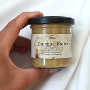 Eine Hand hält ein 125g-Glas mit Omega 3 Butter I Walnussmus von Luke Jaque-Rodney mit deutschem Text. Der cremige Aufstrich wird aus gekeimten Walnüssen in bester Rohkostqualität hergestellt und kommt mit einem schwarzen Deckel.
