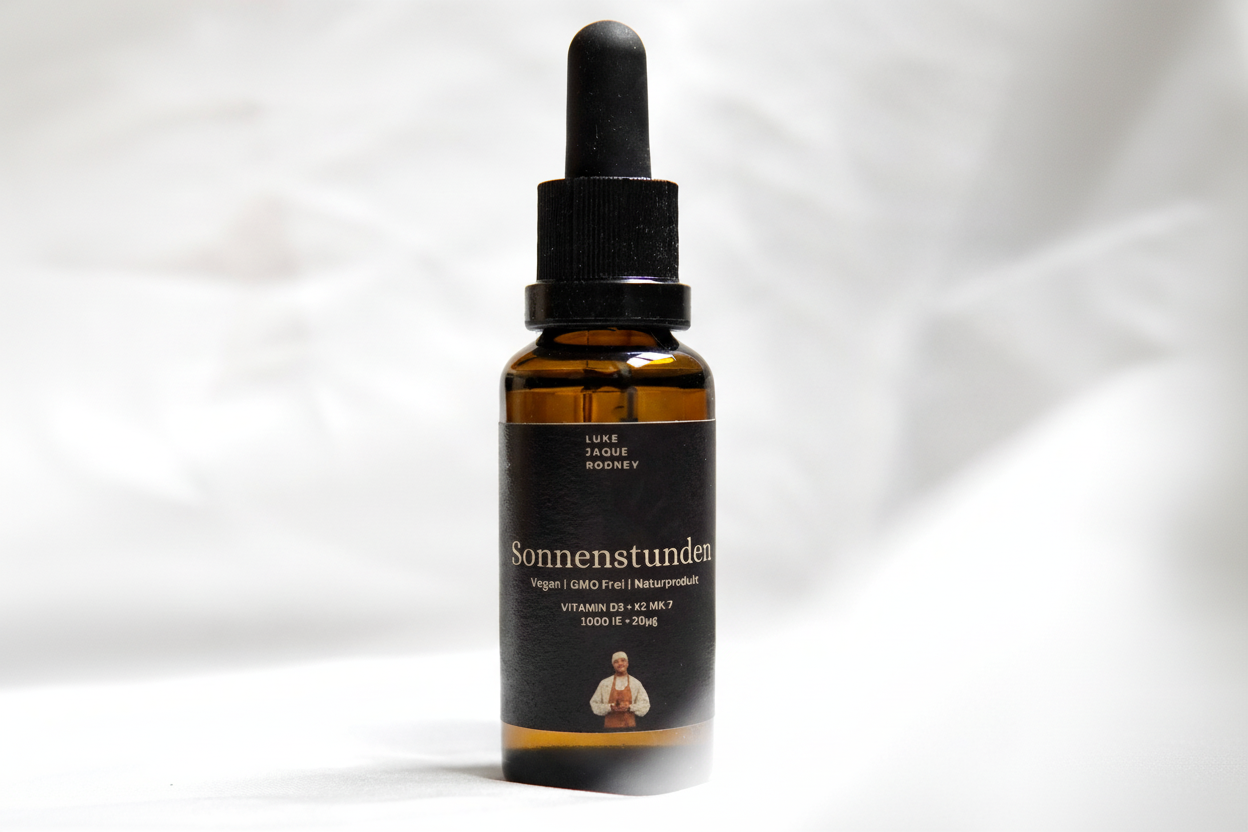 Eine braune Tropfflasche mit der Aufschrift Sonnenstunden I VITAMIN D3 + K2 MK-7 von Luke Jaque Rodney Store, mit dem Text: hoch bioverfügbares, veganes, pflanzliches Vitamin D3K2, GMO-frei. Schwarze Sprechblase: Hält 2-3 Monate!.
